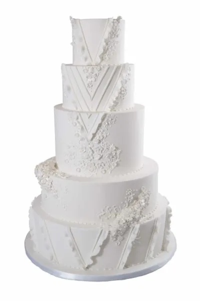 A five-tier white wedding cake featuring elegant lace and floral sugar decorations.