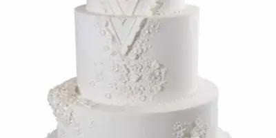 A five-tier white wedding cake featuring elegant lace and floral sugar decorations.