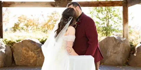 A bride and groom sharing a kiss under a wooden pavilion structure during a wedding ceremony.