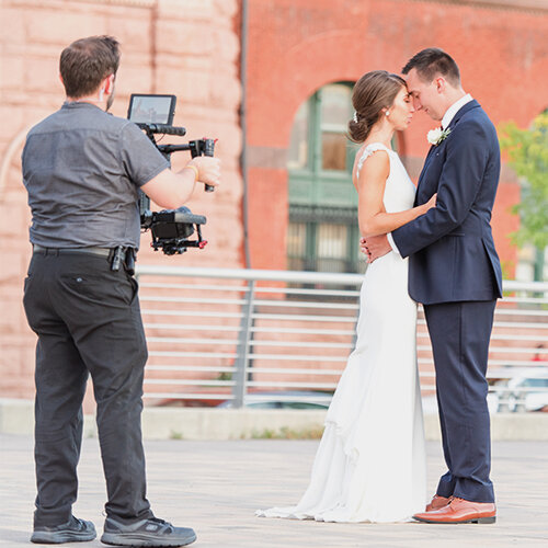 A videographer filming a bride and groom with a professional camera rig.