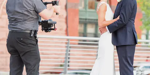 A videographer filming a bride and groom with a professional camera rig.