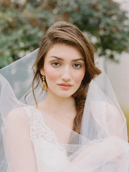 Portrait of a bride with natural makeup and loose, wavy hair wearing a veil.
