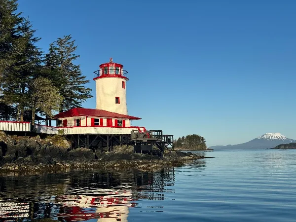 A white and red lighthouse structure on a rocky shoreline with a mountain in the background.