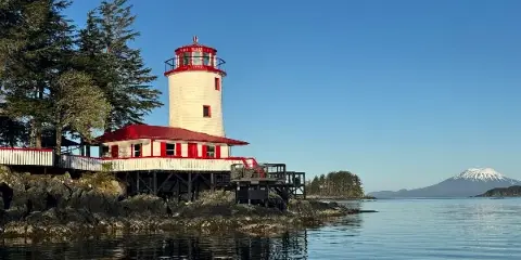 A white and red lighthouse structure on a rocky shoreline with a mountain in the background.