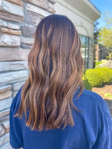 Back view of a client with wavy, balayage hair color standing outdoors.