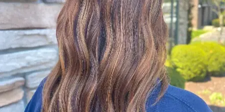 Back view of a client with wavy, balayage hair color standing outdoors.