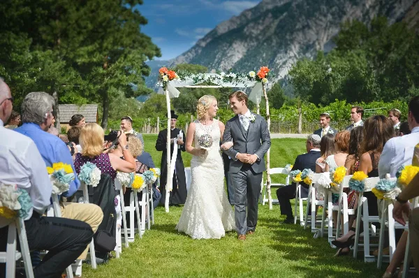 A bride and groom standing at an outdoor wedding altar with guests seated in rows of white chairs.