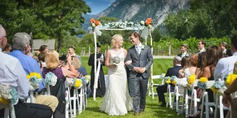 A bride and groom standing at an outdoor wedding altar with guests seated in rows of white chairs.