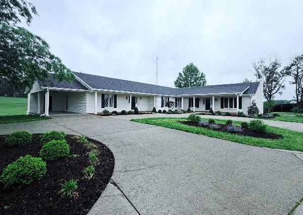 Exterior view of the Blueberry Inn & Spa building at The Buchanan Estate, featuring a white single-story structure with a paved driveway and landscaped grounds.