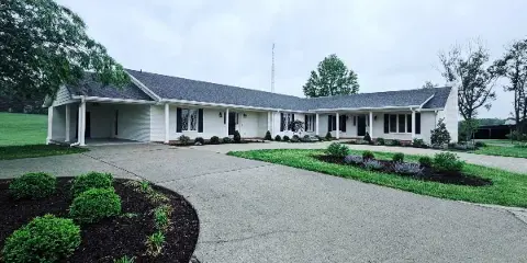 Exterior view of the Blueberry Inn & Spa building at The Buchanan Estate, featuring a white single-story structure with a paved driveway and landscaped grounds.
