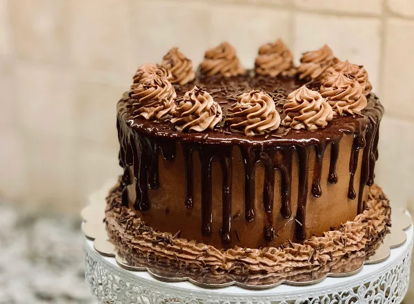 A chocolate celebration cake with dripping ganache and piped frosting swirls on a white cake stand.