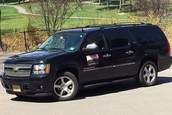 A black Chevrolet Suburban SUV parked on a paved surface with a grassy area in the background.