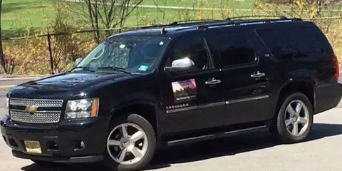 A black Chevrolet Suburban SUV parked on a paved surface with a grassy area in the background.