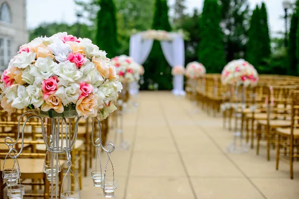Outdoor wedding aisle setup with gold chairs, floral centerpieces, and a white draped archway.