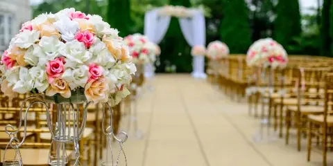 Outdoor wedding aisle setup with gold chairs, floral centerpieces, and a white draped archway.