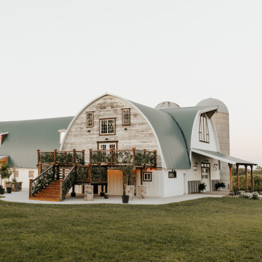 Exterior view of a rustic barn wedding venue with a green arched roof and wooden deck.