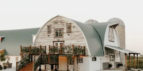Exterior view of a rustic barn wedding venue with a green arched roof and wooden deck.