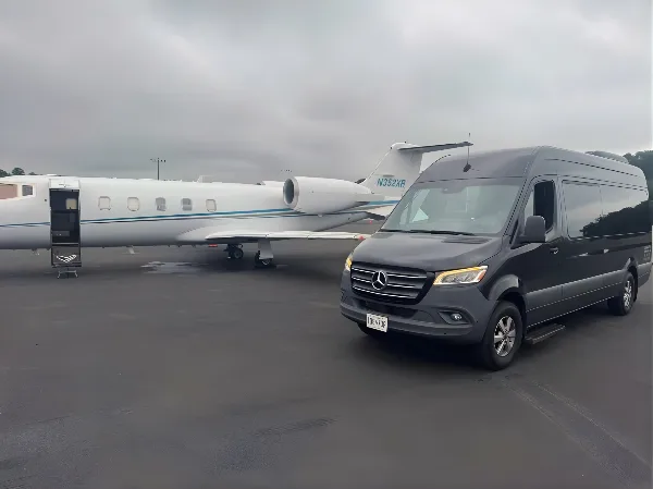 A black Mercedes Sprinter luxury shuttle van parked on an airport tarmac next to a private jet.