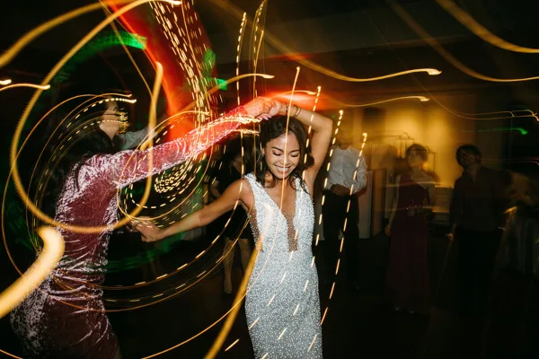 A bride in a white dress dancing joyfully at a wedding reception with light trails in the background.