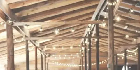 A large group of guests seated at long tables in a rustic wooden venue with string lights.