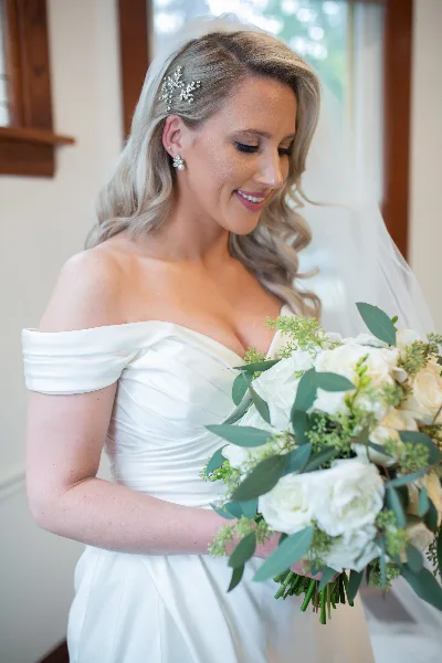 A bride with styled blonde hair and makeup holding a white floral bouquet.