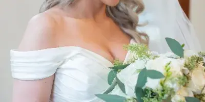 A bride with styled blonde hair and makeup holding a white floral bouquet.