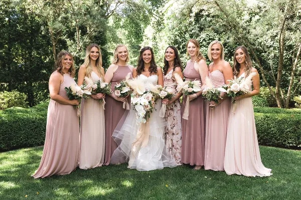 A bride and six bridesmaids in pastel dresses standing outdoors holding bouquets.