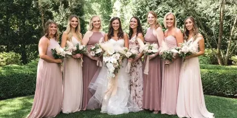 A bride and six bridesmaids in pastel dresses standing outdoors holding bouquets.