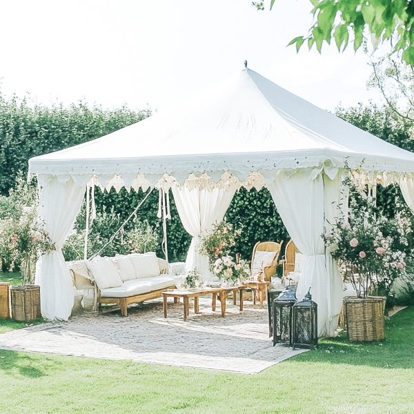 A white event tent set up on a lawn with white draping, a sofa, and floral arrangements.