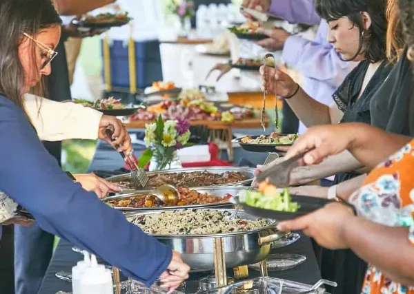 Guests serving themselves food from a buffet line at a catering event.