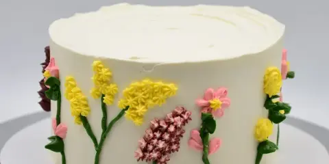 A white frosted cake decorated with yellow, pink, and red piped flowers and green stems.