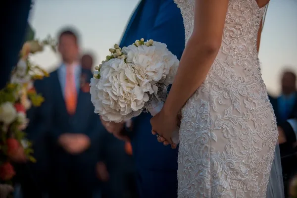 A bride in a lace wedding dress holding a white bouquet during a ceremony.
