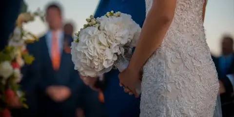 A bride in a lace wedding dress holding a white bouquet during a ceremony.