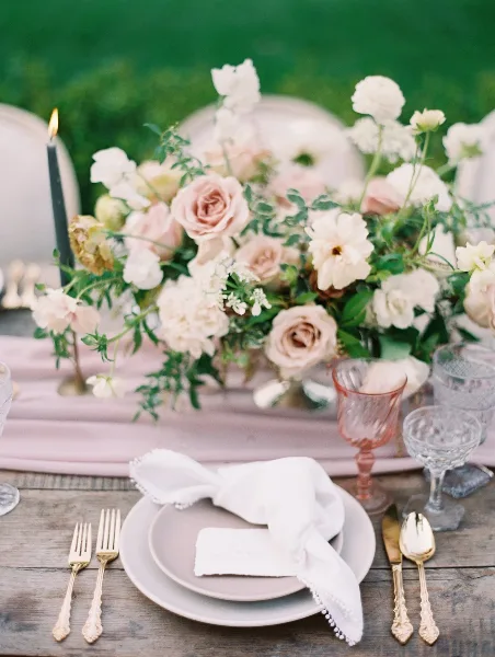 Styled event table with floral centerpiece, pink linens, glassware, and place settings