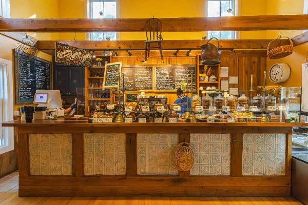 Interior view of a bakery counter displaying pastries, cakes, and chalkboard menus with a wooden service counter and glass display cases.
