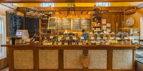 Interior view of a bakery counter displaying pastries, cakes, and chalkboard menus with a wooden service counter and glass display cases.