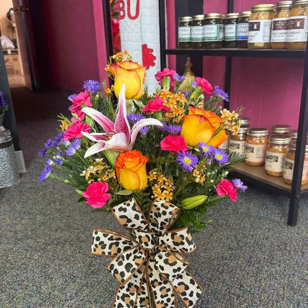 A mixed floral bouquet featuring yellow roses, a pink lily, and pink carnations, tied with a leopard-print ribbon bow.