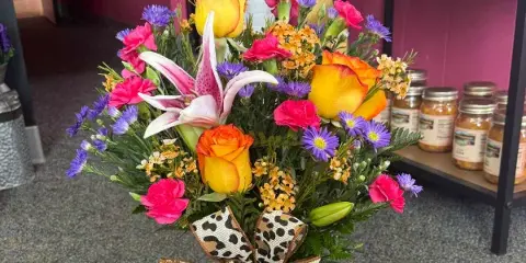 A mixed floral bouquet featuring yellow roses, a pink lily, and pink carnations, tied with a leopard-print ribbon bow.