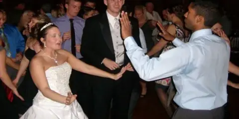 A bride and groom dancing at a wedding reception with other guests in the background.