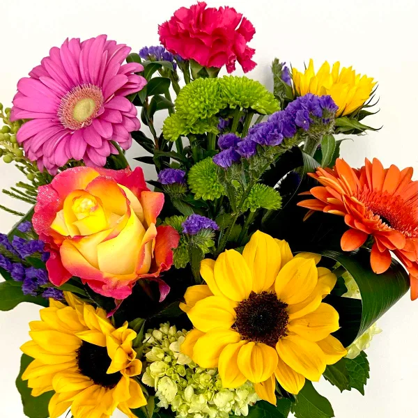 A colorful floral arrangement featuring sunflowers, pink and orange gerbera daisies, a rose, and greenery.
