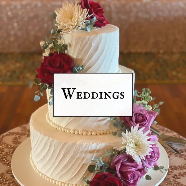 A three-tier white wedding cake decorated with red and purple roses, white chrysanthemums, and eucalyptus greenery.
