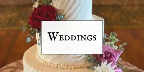A three-tier white wedding cake decorated with red and purple roses, white chrysanthemums, and eucalyptus greenery.
