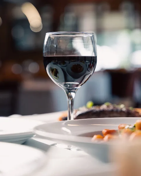 A glass of red wine and plated food on a restaurant table.