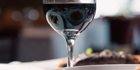 A glass of red wine and plated food on a restaurant table.