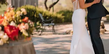 A bride and groom kissing outdoors next to a wine barrel during a wedding ceremony.