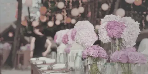 A long event table set with white linens, glassware, and large floral centerpieces in a decorated venue.