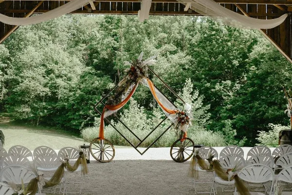 A wedding ceremony setup with a floral arch and white chairs under a wooden pavilion structure.