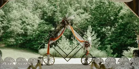 A wedding ceremony setup with a floral arch and white chairs under a wooden pavilion structure.