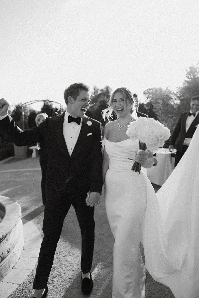 Black and white photo of a bride and groom laughing and walking hand-in-hand after their wedding ceremony.