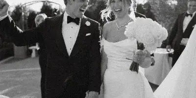 Black and white photo of a bride and groom laughing and walking hand-in-hand after their wedding ceremony.
